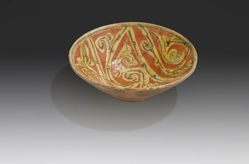 Coupelle aux rinceaux de bambou sur fond brique, Transoxiane, Xe siècle Coupelle en céramique argileuse, à décor engobé de rinceaux de demi-palmettes et tiges de bambou en réserve sur fond brique, sous glaçure transparente. D.: 12,5 cm - H.: 4 cm État: fractures recollées. A pottery bowl with a bamboo design, Tansoxania, 10th century