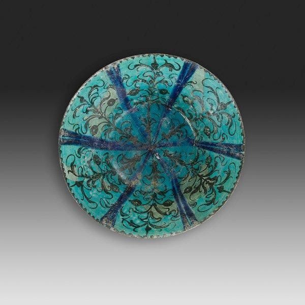 Coupe aux tiges végétales, Iran, Kachan, XIIe - XIII siècle Coupe tronconique en céramique siliceuse à décor peint en noir sur glaçure colorée en turquoise. Décor rayonnant de tiges végétales séparées par des lignes bleues. Au revers, frises de fleurons. Diam.: 20,5 cm; H.: 8,5 cm État: anciennes restaurations

A glazed pottery bowl, Iran, Kashan, 10th - 13th century