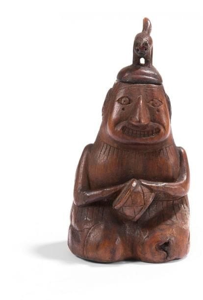 Poporo représentant une femme shaman. Assise sur ses pieds, elle joue du tambour pour rentrer en transe. L?expression de son visage indique la prise de substance hallucinogène. Des nattes retombent dans le dos et encadrent un motif solaire. Un félin se dresse sur la tête. Ce petit objet est d?une grande finesse d?exécution. Chaque détail est minutieusement gravé et donne vie à ce personnage. Bois gravé à patine brune. Culture Chiribaya, Pérou 900 - 1200 ap. J.-C. H: 9,8 cm - l: 5 cm - Ep: 5 cm Provenance: Collection privée, France