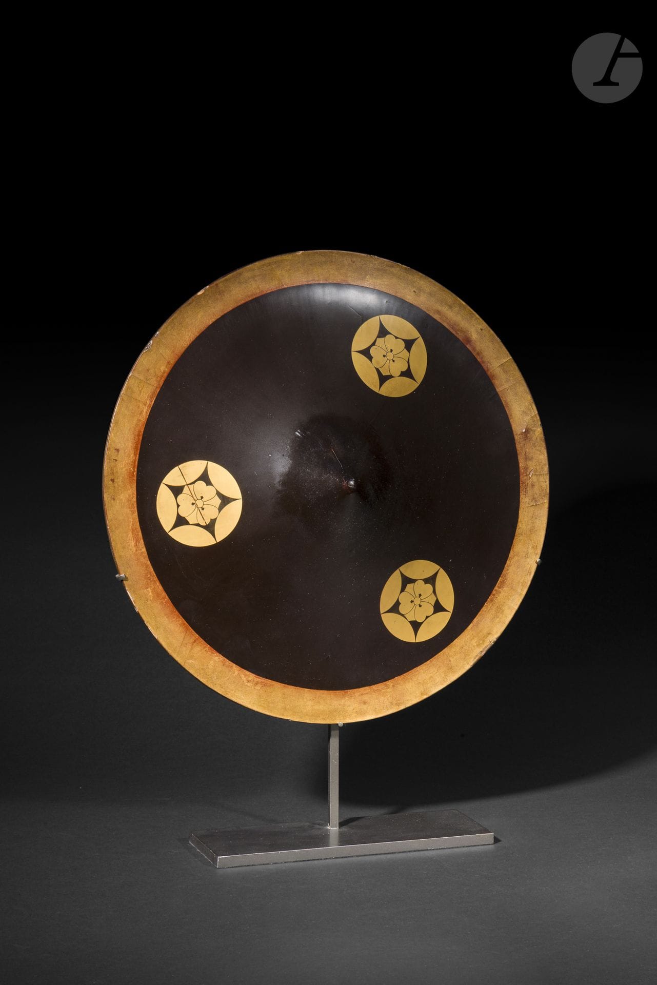 Jingasa de type ichimonji, Japon, époque Edo, XIXe siècle
En harikake laqué noir et or à décor de trois mon de type shippo ni ken katabami. Le bord de la jingasa est laqué or et l’intérieur est laqué rouge avec un décor en kirikane or.
Diamètre : 42,5 cm
Quelques manques, restauration au sommet de la jingasa.