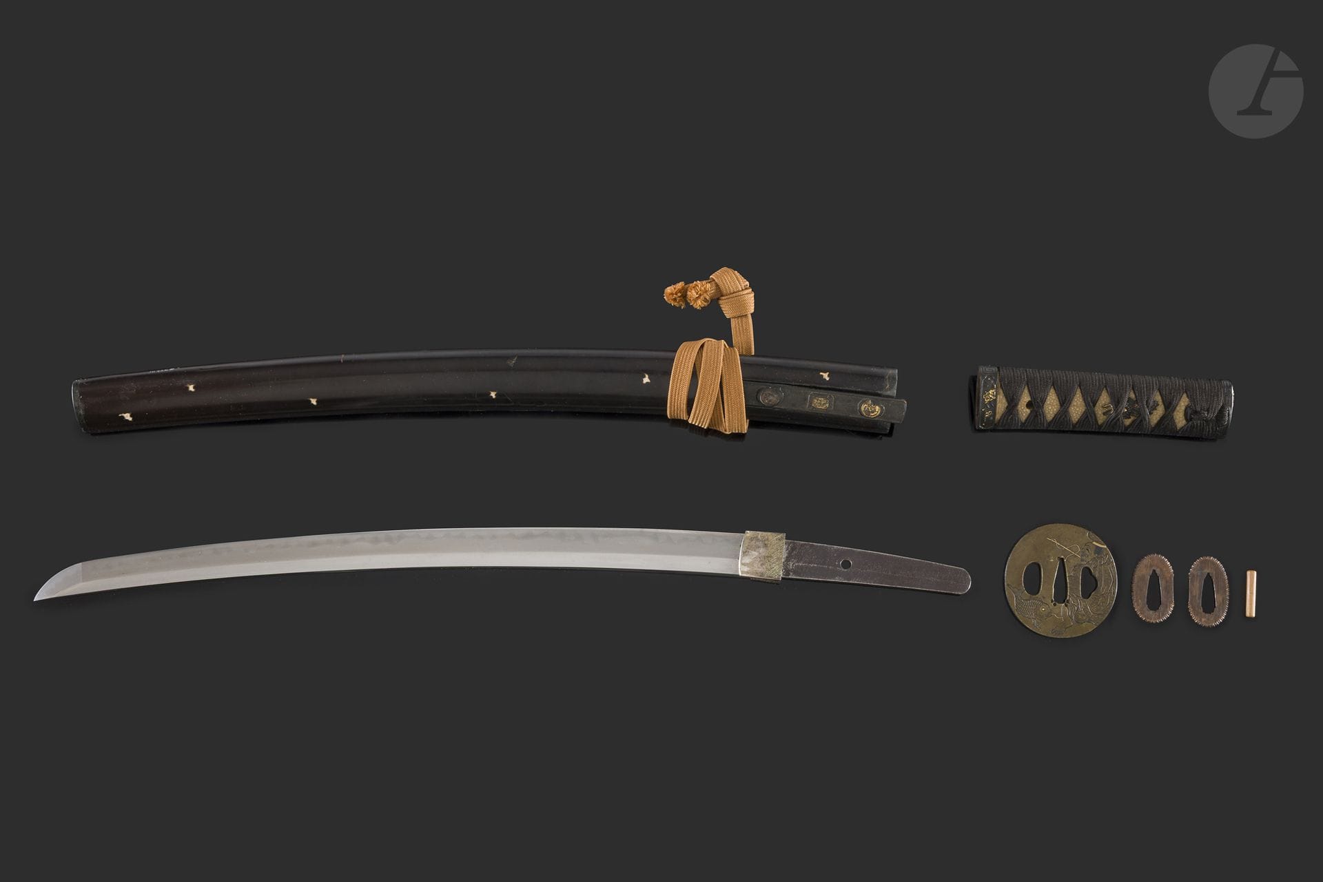 Wakizashi et son koshirae, Japon, fin de l’époque Edo (1603-1868)
Lame shinogi zukuri, ji koitame hada, hamon mélange de gunome midare et choji midare. Gimei porte une signature Bishu Osafune Yasumitsu. Nagasa : 40,6 cm. Koshirae composé d’une tsuka lacée noir, fuchi kashira en shakudo à fond nanako à décor, ciselé en haut relief et doré, de prunier en fleurs. Tsuba en sentoku ciselée en katakiribori d’Ebisu pêchant un poisson et au revers de vagues écumantes. Une signature ciselée Kuwamura Genzaemon Katsuhisa avec kao - 桑村源左衛門　克久. Saya en bois laqué noir avec des shidori en coquillage incrustés.