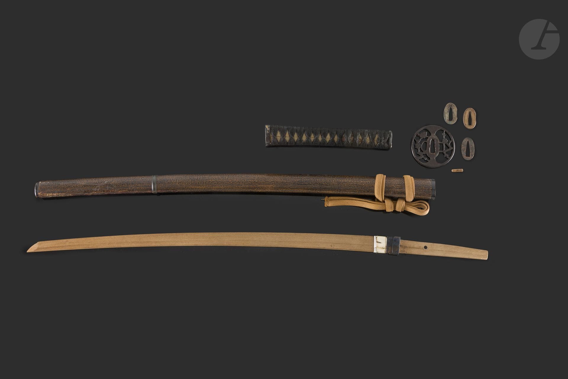 Koshirae complet avec tsunagi, Japon, époque Edo/Meiji
Il est composé d’une tsuka recouverte de same, lacée noir avec un fuchi kashira en shakudo décoré en iroe taka zogan de feuilles, rinceaux et cucurbitacés. Menuki en suaka représentant deux suzume (moineaux). Tsuba maru gata en fer à décor en sukashi d’un uguisu (rossignol) dans des branches de prunier en fleurs. Saya en bois laqué noir et brun clair imitant l’écorce du bois avec un kurikata sur lequel est noué un sageo ocre.
Long. totale : 70,5 cm
Réparation sur le saya.