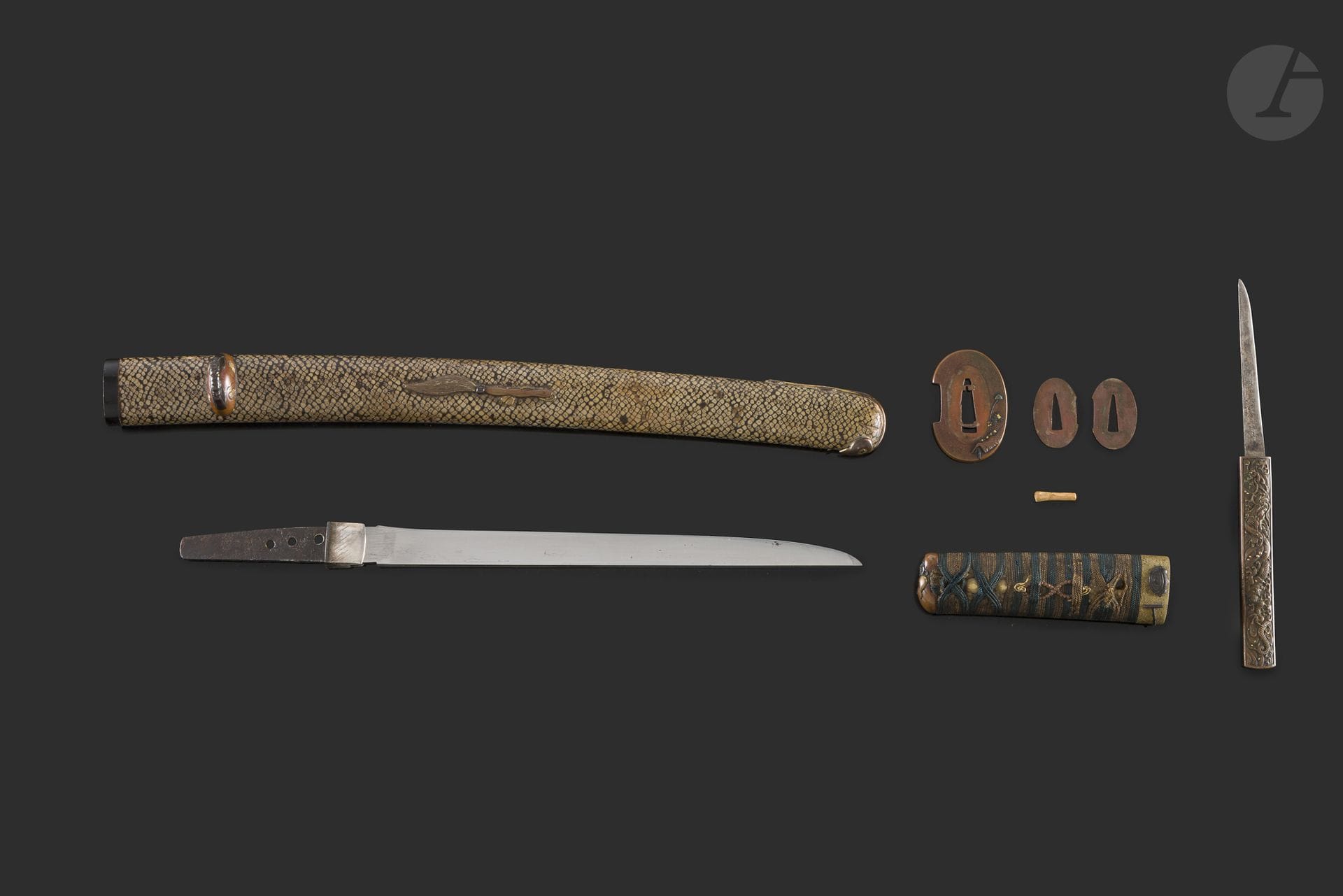 Sabre d’enfant, Japon, époque Edo (1603-1868)
Lame hira zukuri à trempe non lisible, koshirae composé d’un saya probablement recouvert de peau de serpent, toutes les montures métalliques sont à sujet de Daruma et ses attributs en suaka, shakudo, et tokin. Kozuka en suaka à décor d’un dragon dans les flots. 
Nagasa : 22,1 cm
Lame usée. Réparation au fourneau.