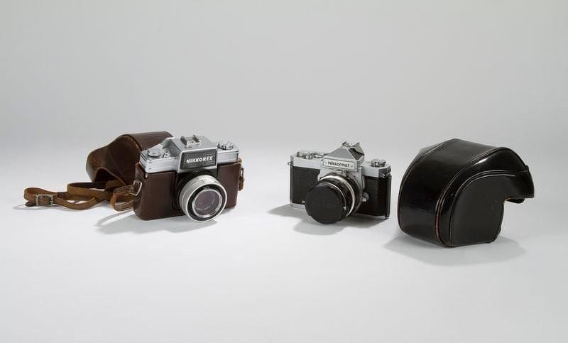 Appareil photographique 24 x 36 mm, Nikon, Nikkormat. Corps métal, partie supérieure satinée gris argent, le reste gainé cuir granité. Objectif Nikkor Auto 1:2, f50m/m. N° Série: FT 3156951. C. 1970. On joint : Appareil 24 x 36 mm, Nikkorex. Corps métal partie supérieure satinée gris argent, le reste gainé cuir granité. Objectif à baïonnette Nikkor Q 1:2,5 f5cm, No 364537, marqué Nippon Kogaku Tokyo. C. 197O.