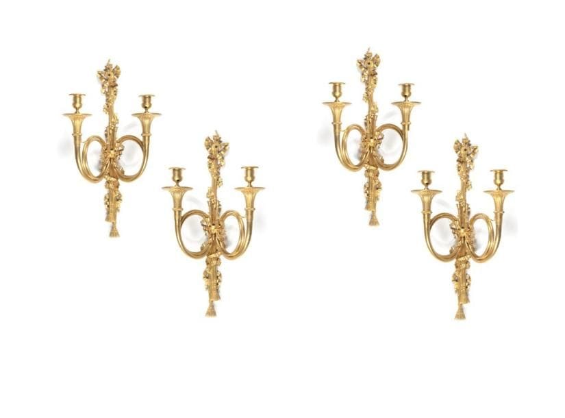 Suite de quatre appliques aux cors à deux lumières en bronze doré, à décor de passementerie, feuilles de lierre et noeud de ruban; percées pour l'électricité. XIXe siècle. Hauteur: 56 cm