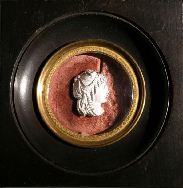 Plaque ronde en cristal, ornée d'une tête de femme à l'antique. Cadre carré en bois noir et jonc doré. Haut. 9,8 cm