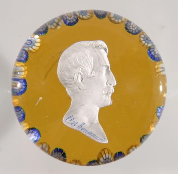 SAINT-LOUIS
Presse-papiers à fond ambre orné d'un cristallo-cérame représentant le profil droit de Louis-Napoléon Bonaparte; couronne périphérique de bonbons jaunes et blancs alternés de bonbons tricolores. Diam. 6,7 cm - Haut. 5,2 cm
