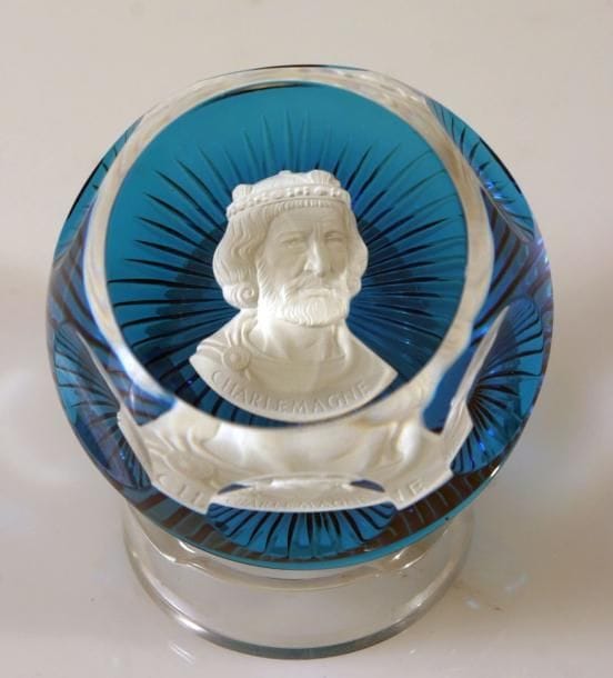 BACCARAT
Presse-papiers à fond bleu translucide orné d'un cristallo-cérame représentant le buste de Charlemagne. Taille à six pontils, fenêtre supérieure et motif rayonnant au revers. Produit en 1976. Diam. 7,4 cm - Haut. 4,4 cm