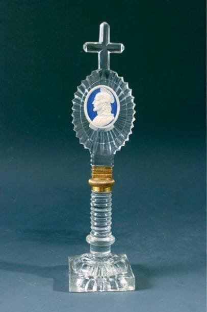 BACCARAT
Ornement sur pied et croix sommitale en cristal taillé de motifs rayonnants et cordons, orné d'une médaille représentant le profil de Jésus sur fond bleu; bague intermédiaire en cuivre doré. Haut. 23 cm