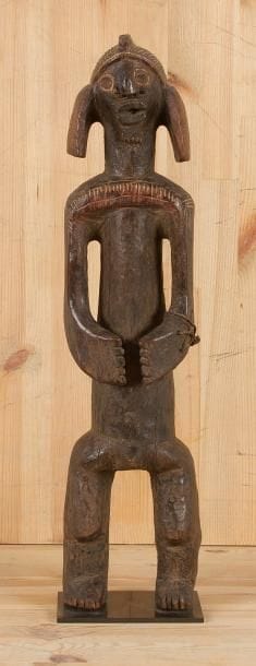 MUMUYE (Nigéria) Sculpture de bonne ancienneté, les bras classiquement enveloppant le tronc, coiffure à crête, lobes d'oreilles non perçés, nez épaté avec labret en bois, bouche lippue, barbe. Patine brune. Circa 1940/1950. (Restauration à la main gauche). Hauteur: 57, 5 cm Provenance: Collection Jacques de Vilmorin, Paris