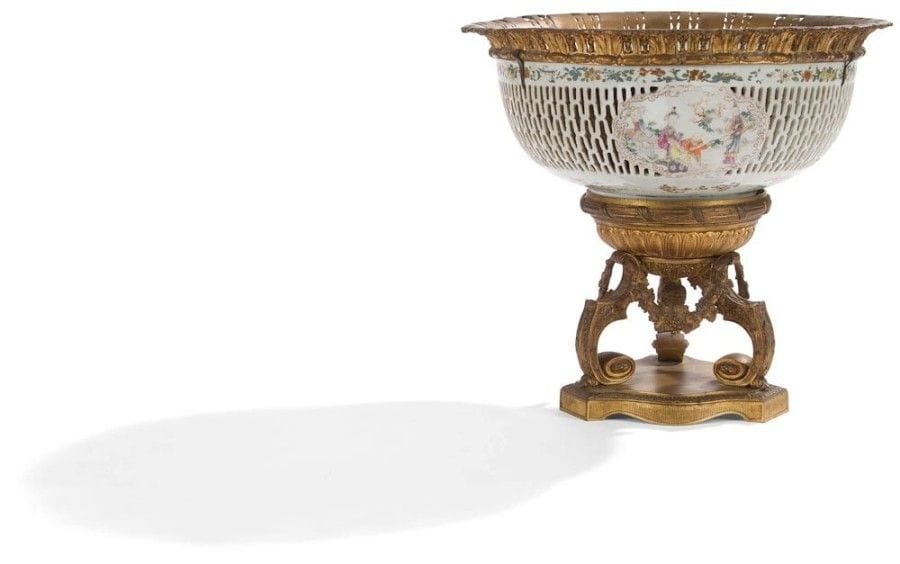 Grande coupe en porcelaine ajourée à décor de personnages chinois reposant sur des montants en volute, la monture ajourée à décor de feuillages, godrons et pomme de pin.
Style Régence.
(Accidents et restaurations). 
H. : 40 cm - D. : 34 cm