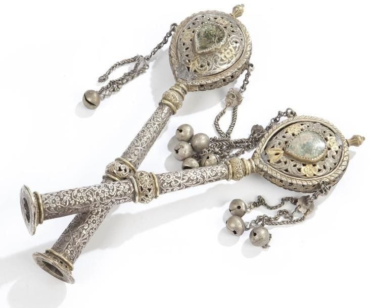 PAIRE DE RIMONIM en métal argenté et doré, fût au décor floral ciselé et têtes autrefois ornées de fixés sous verres (absents ou brisés). Orient, XIXe siècle Hauteur: 25 cm Manque 3 clochettes sur l'un.
