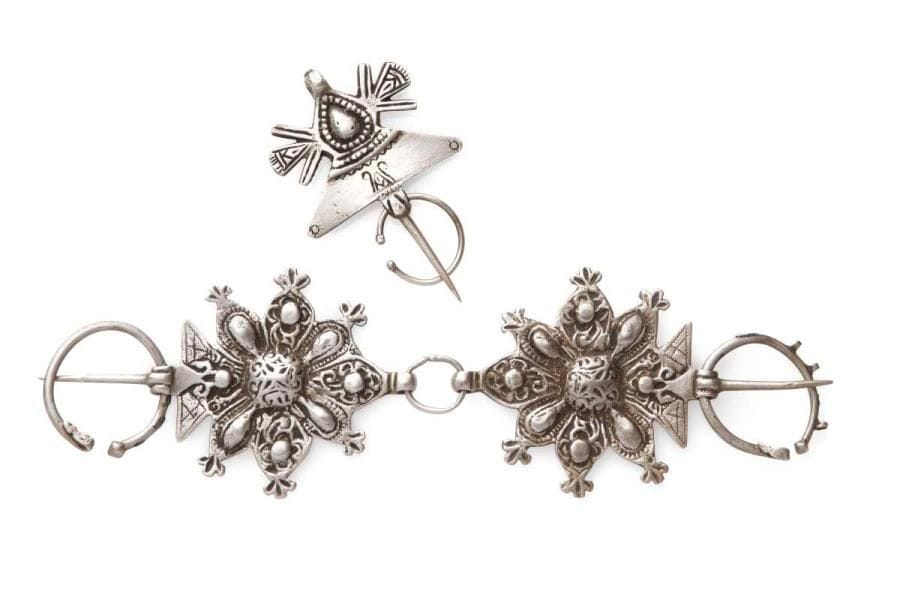 Paire de fibules et fibule en argent, Maroc, tribu du Haut Altas, Dadès et vallée du Draa, fin XIXe-début XXe siècle Paire de fibules à décor ciselé, repoussé et niellé, en forme de rosette fleuronnée. La fibule à mandorle moulée et niellée. Long.: 29,5 cm et 11 cm PB.: 189 g et 75 g Three silver fibulae, Morocco, High Atlas Tribe, Dades and Draa valley, late 19th - early 20th century
