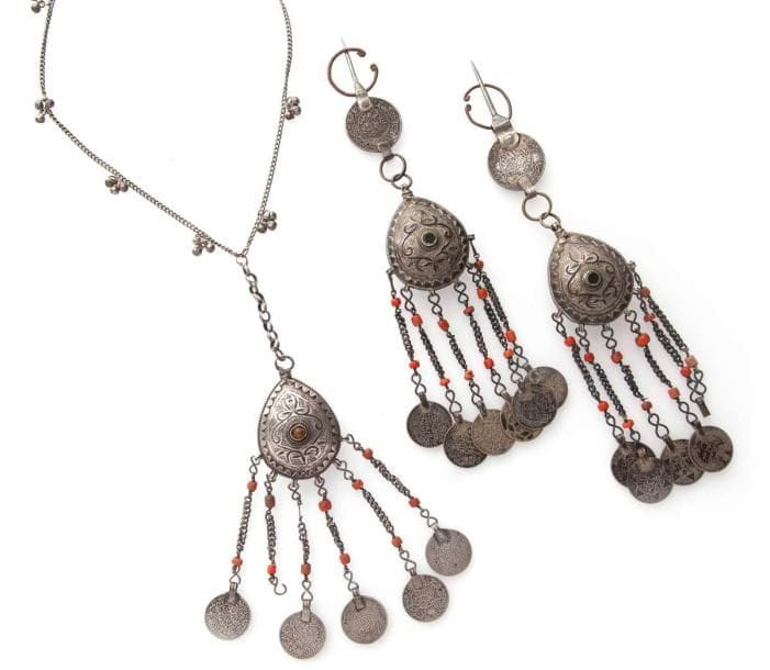 Trois fibules zaïane en argent, Maroc, Moyen Atlas, XXe siècle Trois fibules à pendentif central bermil au décor ciselé et niellé de fleurons à cabochon de verre. Pendeloques à pièces de monnaies datées 1320 - 1336 H. / 1902-1917 avec poinçon du bélier sur chacune, la dernière montée en collier. Le bermil, pendentif en forme de poire aux faces bombées et décorées, serait une parure caractéristique des Berbères zaïane, de la bordure orientale du Plateau central marocain. Long.: 24 cm et 47 cm (avec le collier) PB.: 191 g et 97 g (avec le collier) État: manque trois pièces de monnaies. Three silver fibulae, Zaïane, Morocco, Middle Atlas, 20th century