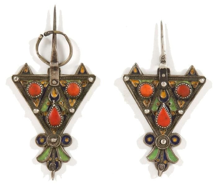 Paire de fibules, abzim, Algérie, Grande kabylie, Benni Yenni, XXe siècle Fibules de forme triangulaire en argent ciselé, décorées d'émaux cloisonnés jaunes, verts et bleus, rehaussées de cabochon de corail. Dim.: 14 cm; 13 cm PB.: 117 g État: manque un anneau sur la plus petite. A pair of triangular silver fibulae,"Abzim", Algeria, Great Kabilya, Benni Yenni,19th century