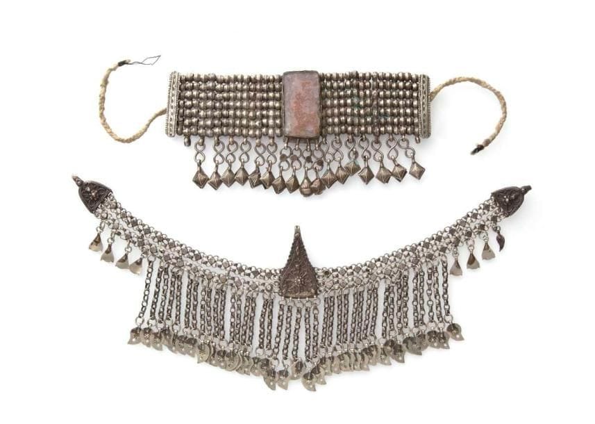 Diadème et collier bédouins en argent, Yémen, XXe siècle Le premier en alliage bas titre formé de deux chaînes perlées, garnies de pendeloques à grelots à attache triangulaire. Le deuxième composé de sept rangées de perles argent présentant une plaque de verre brun. Long.: 37 cm; 19 cm (sans bandeau de coton) Larg.: 11,5 cm; 9 cm PB.: 141 g; 227 g A head set and a necklace, Yemen, 20th century
