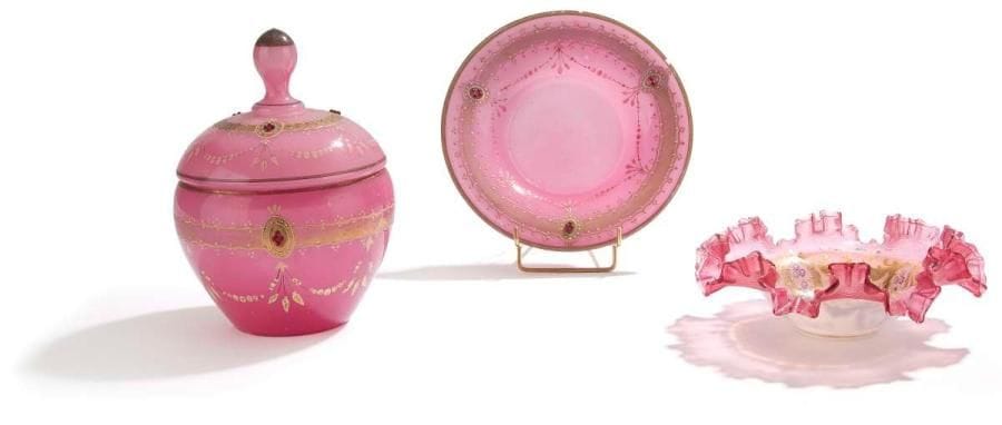 Bonbonnière couverte et coupe en opaline rose, Iran, fin XIXe siècle Bonbonnière couverte et sa soucoupe en verre rose, ornée de rinceaux floraux dorés et de médaillons de petites perles de verre rouge. Coupe en opaline, à bord plissé et ondulé, à décor central de quatre médaillons à feuilles d'acanthes dorées. H.: bonbonnière couverte: 25 cm; coupe: 7 cm An opaline covered sugar bowl with its plate and a cup, Iran, late 19th century