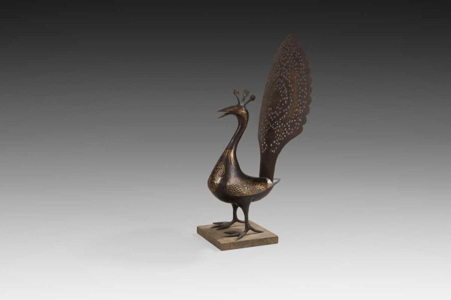 Paon en acier, Iran qâjâr, XIXe siècle Ronde-bosse en acier, reposant sur un socle, décor peint en or soulignant le plumage des ailes, un médaillon végétal sur le poitrail, deux paons sur la queue réticulée. H.: 41 cm; long.: 16 cm A steel peacock, Qajar Iran, 19th century