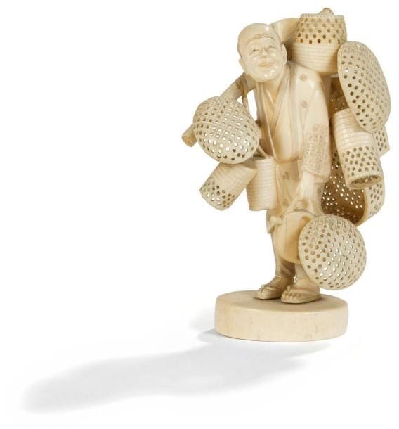 JAPON - Epoque MEIJI (1868 - 1912)
Okimono en ivoire à patine jaune représentant un colporteur debout portant des paniers et lampions. (Parties détachées). Haut.: 14,5 cm