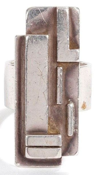 Jean DESPRES (1889-1980)
Bague moderniste en argent. Le large anneau, traité lisse, reçoit une plateforme excentrée rectangulaire au décor de motifs géométriques en application sur un fond martelé. Signé J. DESPRÉS à la pointe au revers et porte les poinçons de Maître Orfèvre et de garantie sur l'anneau. Poids: 23,07 g