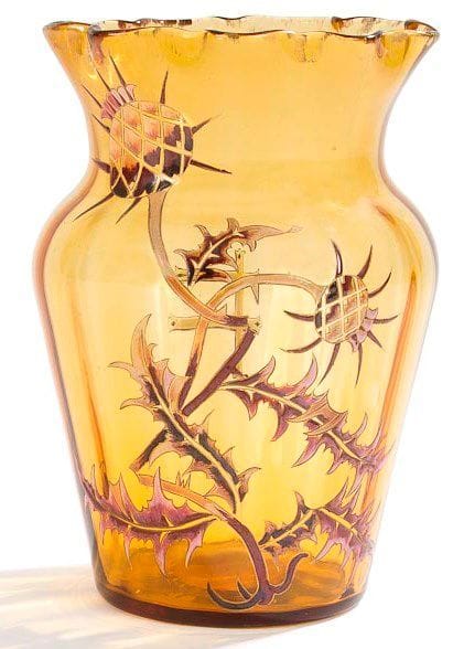 Émile GALLÉ (1846-1904)
Haut vase balustre légèrement côtelé à col festonné. Épreuve en verre ambré au décor aux émaux polychromes de chardons sur une face et d'une Croix de Lorraine sur l'autre. Riches rehauts de dorure dans le décor et en pourtour du col. Usures à la dorure du col. Signé et situé E. GALLÉ à Nancy à l'or (en partie effacé) sous la base. Hauteur: 27 cm