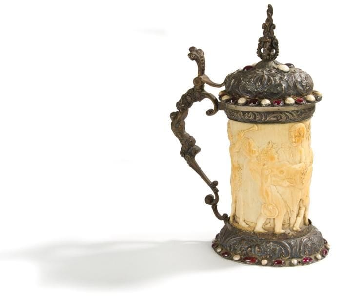 Chope en ivoire, monture en argent et métal argenté avec cabochons de verroterie. Décor d'une bacchanale avec cortège d'enfants monture avec coquilles et rinceaux, fruits, anse formée d'un homme engainé mangeant des raisins Allemagne, XIXe siècle dans le style de la Renaissance Hauteur: 21 cm. (légers manques aux verroteries)