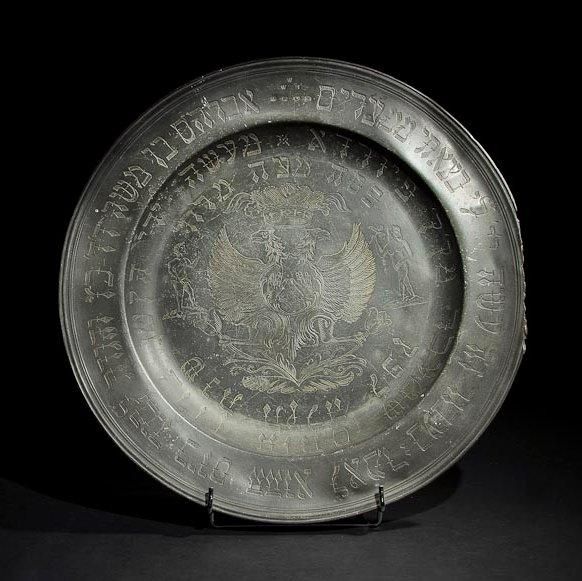 PLAT DE PESSAH Allemagne, Fürth, XVIIIe siècle, daté en hébreu 1775. Étain gravé. Diamètre: 46.5 cm
Plat portant sur l'aile le verset biblique enjoignant de raconter à son fils la sortie d'Égypte ainsi que le nom du propriétaire du plat: Abraham fils de Moïse D.D. Katz. Entre l'aile et le bassin figurent en hébreu, le nom du graveur, son origine et la date:[Gravé des mains? de Baroukh Hotem Stacher de la ville de Furth Année 1775] Le plat est décoré au centre d'un aigle bicéphale couronné autour des mains du Cohen (prêtre) ouvertes pour la bénédiction. Les deux mains rappellent que le propriétaire du plat est un Cohen. De part et d'autre de l'aigle sont représentés Adam et ève. Usures et manques. Mots-clés: Judaica, Jewish, Hebrew, Judaïsme, Hébreu.
Passover Plate. Germany, Furth, 18th century, dated in Hebrew 1775. Engraved pewter.