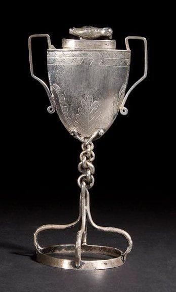 BOÎTE À AROMATES Autriche-Hongrie, XIXe siècle. Argent fondu, gravé et ciselé. Poinçons: 11 et poinçon d'orfèvre JLR. Hauteur: 13 cm Poids: 56 g
Curieux compartiment à aromates en forme d'urne au couvercle muni d'une prise en forme d'oiseau. Cette urne repose sur un pied formé d'une base représentant une couronne. Les quatre tiges courbes qui la composent se rejoignent sous l'urne et s'entrelacent pour former une natte. Mots-clés: Judaica, Jewish, Hebrew, Judaïsme, Hébreu.
Spice Box. Austria-Hungary, 19th century. Cast, engraved/chased silver. Hallmarks: 11. Maker's mark: JLR.