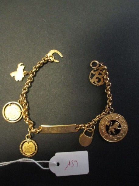 Bracelet gourmette en or jaune 18K, retenant en pampille 7 charms en or 18K: un fer à cheval, une carte du Venezuela, deux pièces de monnaie, un cadenas, une médaille astrologique et un chiffre porte-bonheur. Longueur: 19 cm - Poids: 19 g