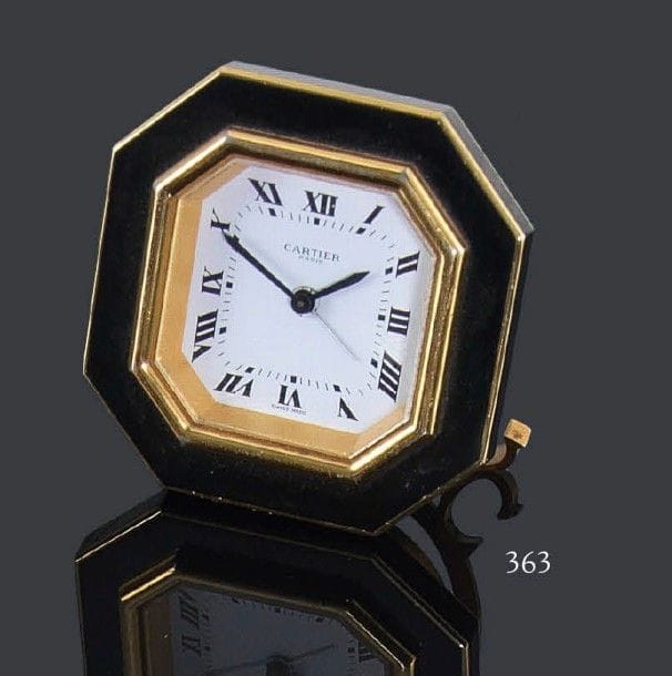CARTIER
Très joli réveil de voyage en laque noire et dorée, carré à angles coupés. Chiffres romains, mécanisme signé Cartier, axe cassé, à réviser. Hauteur: 7,5 cm