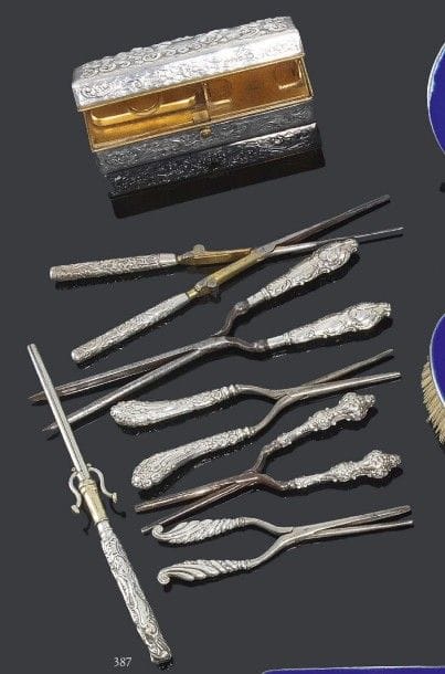 Étonnante collection de seize fers à friser manche en argent à décor repoussé pour la plupart de motifs feuillagés et enroulements, une boîte rectangulaire à chauffer les fers en laiton recouvert d'argent et une petite brosse en crins et manche argent. Angleterre, villes de Londres et Birmingham, fin du XIXe siècle, début du XXe (plusieurs lettres-date et différents orfèvres). Poids brut: 1906 g