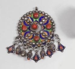 Fibule tabzimt, Algèrie, Grande Kabylie, Beni Yenni, XXe siècle. 
Fibule ronde, en argent, émaillée sur fond vert et jaune de cercles bleus à c?ur floral jaune et vert alternant avec des cabochons de corail, bordée de perles appliquées. 
Diam.: 8.5 cm
P.B.: 182 g
An enamelled silver fibulae,Algéria, Great Kabylia, Bani Yenni, early 20th century