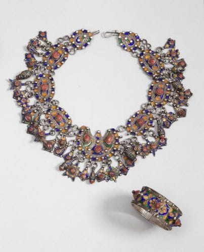 Collier tazlagt et bracelet en argent, Algérie, Grande Kabylie, Beni Yenni, XXe siècle.
Neuf plaques, dont la centrale en argent, émaillée bleu, jaune et vert, à pendeloques diverses en étoiles, tonnelets, gouttes et cabochons de corail ; - Bracelet à charnière, émaillé bleu vert et jaune à cabochons en dômes perlés ou de corail. 
Long collier: 45.5 cm ; Diam. bracelet: 5.5 cm 
P.B.: 345 g
Enamelled silver necklace with pendants and bracelet, Great Kabylie, Beni Yeni, early 20th century 