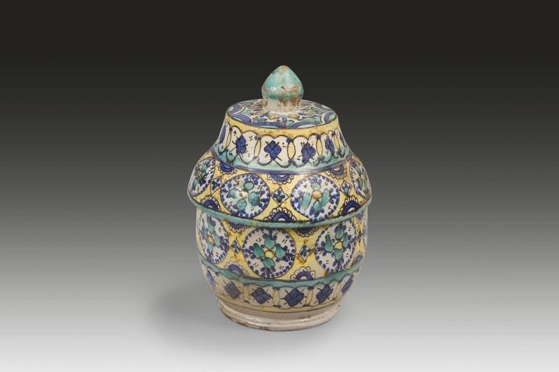 Pot à beurre jobbana, Fès, fin XIXe siècle. 
Faïence jaune, bleu, vert, brun à panse sphérique et couvercle à bouton conique. Décor sur fond jaune, de deux registres de médaillons ceinturés de points bleus à c?ur de fleurs stylisées, encadrés par deux registres à médaillons entrelacés à fleurs bleues.
Haut.: 27.5 cm ; Diam.: 17 cm 
État: éclats
A polychrome pottery butter pot, Jobbana, Morocco, Fez, late 19th century