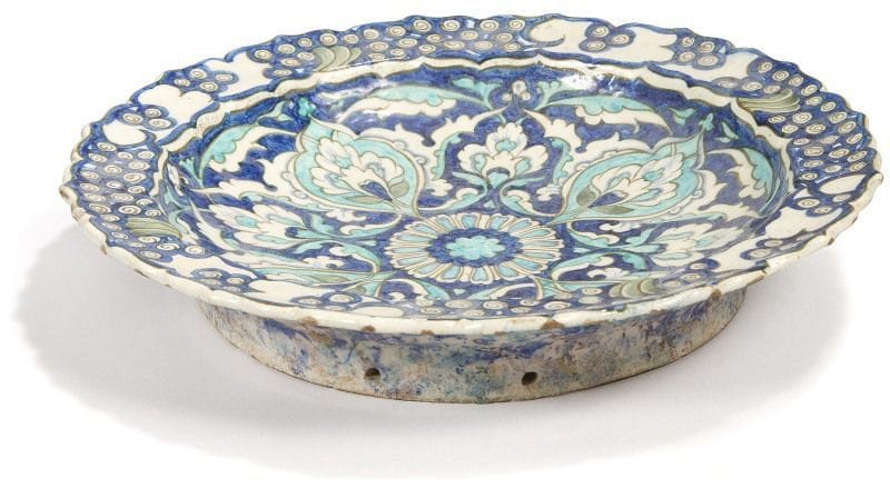 LACHENAL Edmond (1855 - 1930)
Plat aux lotus en boutons, dans le style d'Iznik, fin XIXe siècle. 
Plat aux bords chantournés, peint en bleu de cobalt, turquoise, vert et noir, à décor de rosette entourée de quatre boutons de lotus, et du motif de «vagues et rochers» au rebord. Marque «LACHENAL 105» au dos, sur la base trous de suspension. 
Diam.: 33,7 cm
État: éclats aux bords
LACHENAL Edmond (1855 -1930), an Iznik style pottery dish, decorated with lotus buds, late 19th century 