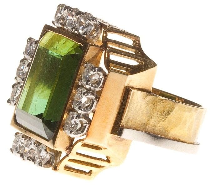 Jean DESPRES (1889-1980)

Spectaculaire bague en or jaune et platine.
L'imposante plateforme, aux flancs ajourés de motifs géométriques, reçoit une tourmaline dans un entourage de diamants sertis.
L'anneau à surface martelée est orné d'un jonc lisse.
Signée J. DESPRÉS à la pointe à l'intérieur de l'anneau et porte le poinçon de garantie.
Poids: 19,46 g
Provenance:
- Madame D., ancienne propriétaire de l'Hôtel de la Poste et du Lion d'Or à Vézelay (Près d'Avallon ? France), ?uvre acquise directement auprès de l'artiste dans sa boutique d'Avallon.
- Par descendance."