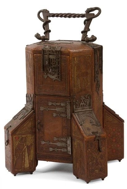 Nathalie MARTIN-SABON (1855-1931) née Nathalie SCHÖNE

Château de cartes, ?uvre unique, 1907
Exceptionnel coffre à jeu(x) de cartes formé d'un corps central octogonal, évoquant la tour maîtresse d'un château médiéval, flanqué de coffrets, simulant des contreforts.
La partie centrale s'ouvre par quatre portes et chaque ailette par un abattant en pente.
Bâti en bois entièrement gainé de cuir au décor repoussé, gravé, poinçonné et, en partie, polychromé et doré, de cartes à jouer figurant les reines, les valets et les couleurs mais aussi de motifs géométriques et de semis floraux.
La partie du dessous, légèrement bombée, est ornée de phylactères recevant des devises en latin.
Les pentures, les entrées de serrure, les encadrements de fente, les fermoirs et la prise, sont exécutés en métal très finement ouvragé ou forgé et évoquent, dans un contexte narratif dans le goût médiéval, les quatre couleurs d'un jeu de cartes.
Les intérieurs découverts par les portes et autres abattants sont gainés en totalité de cuir.
Le dessous, également paré de cuir, reçoit une série de quatre pieds en métal sous chacun des contreforts formant coffrets.
Signé et daté N. MARTIN-SABON 1907, à la base de la partie centrale.
48 x31 x 31 cm
Exposition:
Salon de la Société des artistes français, Paris, 1907 ? Cette ?uvre fut présentée lors de cette manifestation.
Bibliographie:
L'Art décoratif ? Janvier à Juin 1907. ?uvre reproduite page 182.
Historique:
Nathalie Martin-Sabon, peintre, sculpteure et relieuse, jouissait de son vivant d'une grande réputation dans ces différentes disciplines. Les musées d'Orsay et Gustave Moreau conservent d'elle de somptueuses reliures. L'artiste cofonda l'Union des dames des Arts décoratifs. Née Schöne, elle épousa Félix Martin-Sabon, qui, ingénieur de formation, abandonna son activité professionnelle pour se consacrer principalement à la photographie des monuments historiques à travers la France entière, plus de quinze mille de ses plaques sont conservées aujourd'hui à