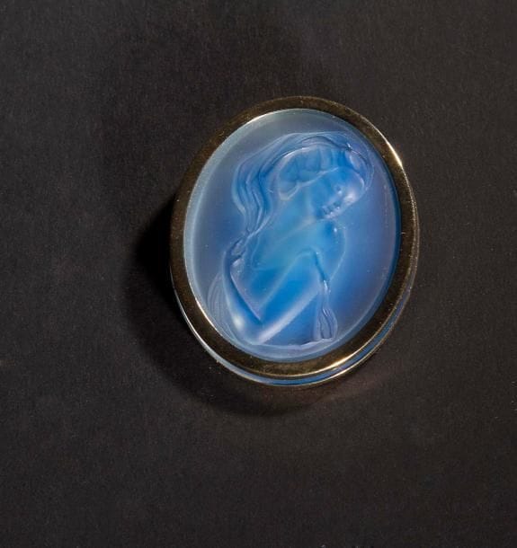 MAISON LALIQUE d'après un modèle de Marie-Claude LALIQUE (1935-2003)

Clémence
Broche médaillon en cristal moulé-pressé, achevé satiné, sur tain miroir bleu. Platine en métal doré. Signée LALIQUE France au revers de la platine. L. 4,5 cm