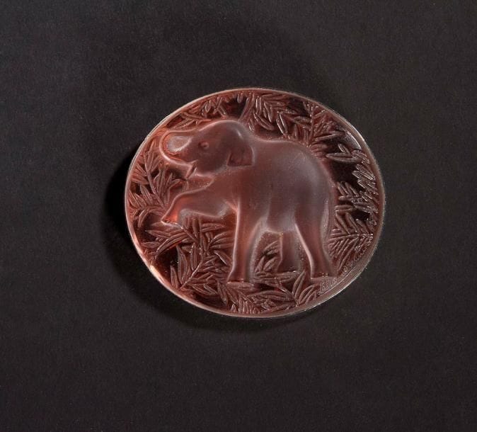 MAISON LALIQUE d'après un modèle de Marie-Claude LALIQUE (1935-2003)

Éléphant
Broche en cristal moulé-pressé, achevé satiné, sur tain miroir rose. Platine en métal argenté. Signée LALIQUE France au revers de la platine. L. 6 cm