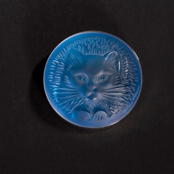 MAISON LALIQUE d'après un modèle de Marie-Claude LALIQUE (1935-2003)

Tête de chat
Broche en cristal moulé-pressé, achevé satiné, sur tain miroir bleu. Platine en métal argenté. Signée LALIQUE au revers de la platine. D. 4,8 cm