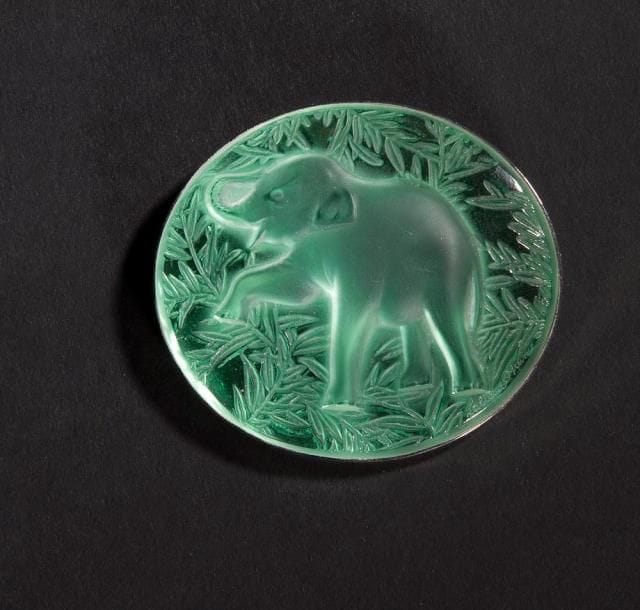 MAISON LALIQUE d'après un modèle de Marie-Claude LALIQUE (1935-2003)

Éléphant
Broche en cristal moulé-pressé, achevé satiné, sur tain miroir vert. Platine en métal argenté. Signée LALIQUE France au revers de la platine. L. 6 cm