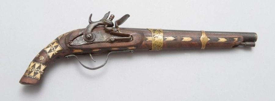 Pistolet à silex africain. 
Canon rond. Garnitures en fer et laiton. Crosse en bois teinté incrusté de morceaux d'os découpés et gravés. Baguette en fer.
XXe siècle. Fabrication locale