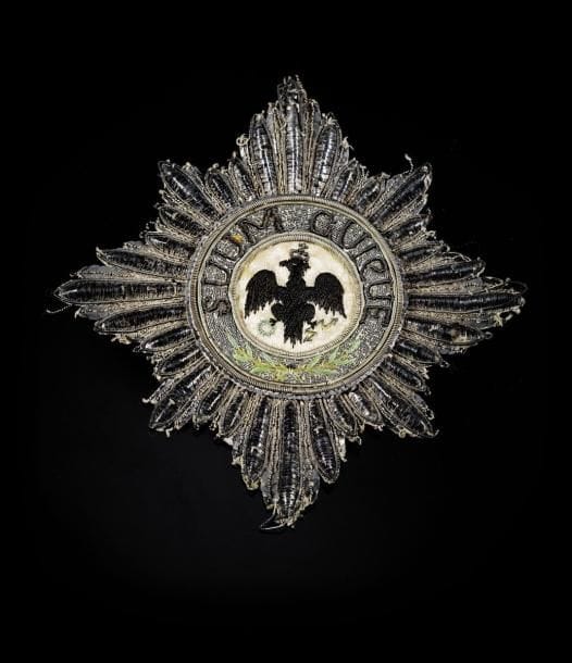 PRUSSE (Royaume)

ORDRE DE l'AIGLE NOIR, fondé en 1701.
Grande plaque de Chevalier.
étoile à huit branches rayonnantes en lamé, canetille et paillettes d'argent.
Centre finement brodé sur fond de fil de soie ivoire, d'un aigle couronné tenant un foudre et une couronne de lauriers, en fil noir, vert et jaune, et canetille argent pour la couronne. Légende sur fond de fil d'argent, brodé de la devise «SUUM CUIQUE», en canetille et paillette d'argent et de branches de lauriers en fil vert et marron. 
Doublée d'origine en papier.
Diamètre: 12,1 cm
T.B. A été portée. époque Premier Empire.(Petits accidents au lamé de deux branches).
Le Maréchal L.A. Berthier a été fait chevalier de l'Ordre de l'Aigle noir le 7 avril 1805 (le même jour que l'Empereur Napoléon Ier).
«Le Roi de Prusse à accordé l'Ordre de l'Aigle-Noir et de l'Aigle-Rouge, à S. M. l'Empereur, au Prince Murat, au Maréchal Berthier, et au général Duroc grand maréchal du palais» Moniteur de 1807.
Provenance: Collections du Maréchal Berthier, Prince de Wagram.
Historique: L'Ordre de l'Aigle noir était l'Ordre honorifique suprême du Royaume de Prusse.
Il fut fondé par le prince-électeur Frédéric III du Brandebourg le 17 janvier 1701, la veille de son couronnement comme premier roi de Prusse sous le nom de Frédéric Ier. Ordre civil et militaire, il ne comprend qu'une classe.
?uvre en rapport:
Portrait du Maréchal Berthier en uniforme de Grand veneur par Andréa Appiani. Musée de Fontainebleau.
Le Maréchal porte sur son habit les plaques de la Légion d'honneur et de l'Aigle noir de Prusse