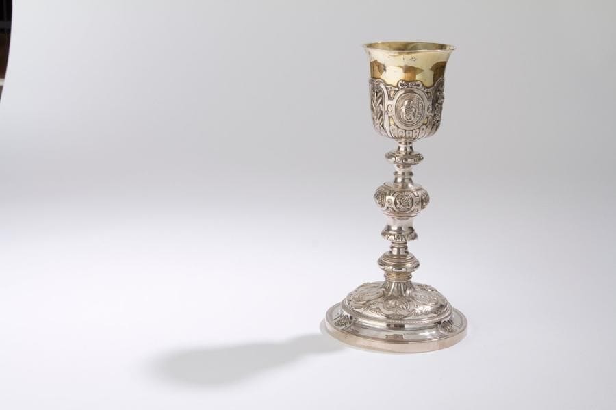 Calice en argent, la fausse coupe en vermeil, sur la base ronde un décor est travaillé au repoussé alternant médaillons de scènes religieuses en rappel sur la monture de la fausse coupe, feuilles de vigne et épis de blé.
Paris 1819 - 1838
Orfèvre: illisible
Poids: 643 g - hauteur: 29,5 cm(*)