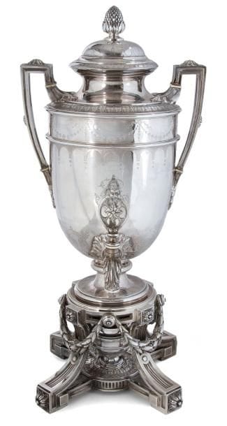 Fontaine à thé en argent fondu ciselé de style Louis XVI en forme d'urne antique en trois parties indépendantes: socle, réchaud et corps. Le socle s'articule autour de quatre pieds cannelés terminés par des rosaces en applique en rappel en partie haute, alternée de festons de guirlandes. Le corps à deux anses latérales est ciselé de rinceaux, le couvercle à doucine terminé par une grenade.
Poinçon minerve
Orfèvre: Odiot, deuxième moitié du XIXe siècle
Poids: support 2641 g - réchaud 133 g - corps 1878 g -
Total net: 4652 g
Hauteur: 53 cm
