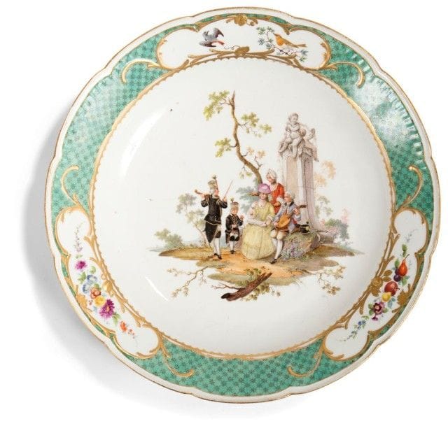 MEISSEN

Plat rond en porcelaine de Meissen, vers 1765, à bord contourné à décor polychrome au centre de deux femmes et un homme dans un jardin assis près d'une fontaine, deux musiciens de la cour de Saxe à leur côté, l'aile à décor polychrome d'oiseaux, fleurs et fruits dans des réserves cernées de rinceaux rocaille en or sur fond vert à treillage. Marqué épées croisées et point en bleu.
Diamètre: 38,5 cm