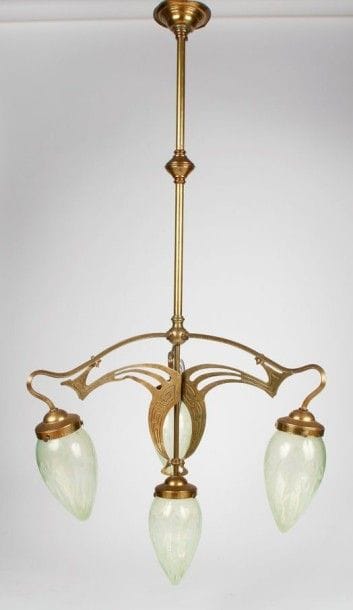 Travail JUGENDSTIL Lustre à quatre lumières réalisé en bronze et laiton à décor de plaques aux motifs sinueux en découpe. Complet de ses quatre tulipes d'origine en verre anisé au décor opalescent de motifs floraux. Vers 1900. H.: 114 cm