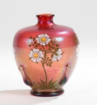 TRAVAIL EUROPÉEN 1900
Petit vase boule sur talon à petit col rétréci ourlé. Épreuve en verre irisé en dégradé de parme et de lie-de-vin, décor émaillé de branches d'églantier en fleurs et d'applications en relief en partie basse. H.: 12,5 cm