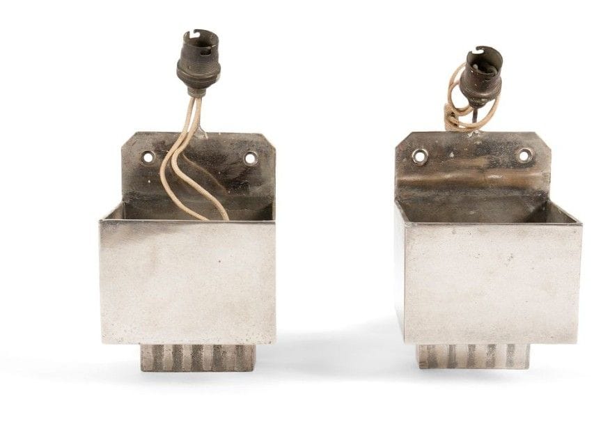 TRAVAIL MODERNISTE Paire d'appliques en métal nickelé. Les structures composées de parallélépipèdes, ceux situés en partie inférieure à décor de cannelures, la source lumineuse dans les parties hautes. Réflecteurs manquants. H.: 21 cm