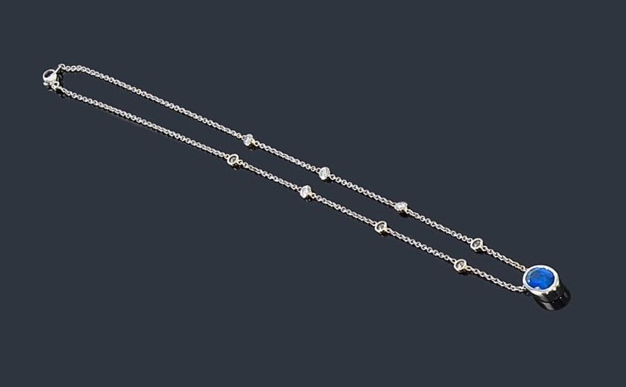 Collier en or gris 18K (750 ?), ponctué de 8 diamants, retenant en pendentif un saphir de forme ovale serti clos. Longueur: 43,5 cm environ. Poids brut: 7,5 g
